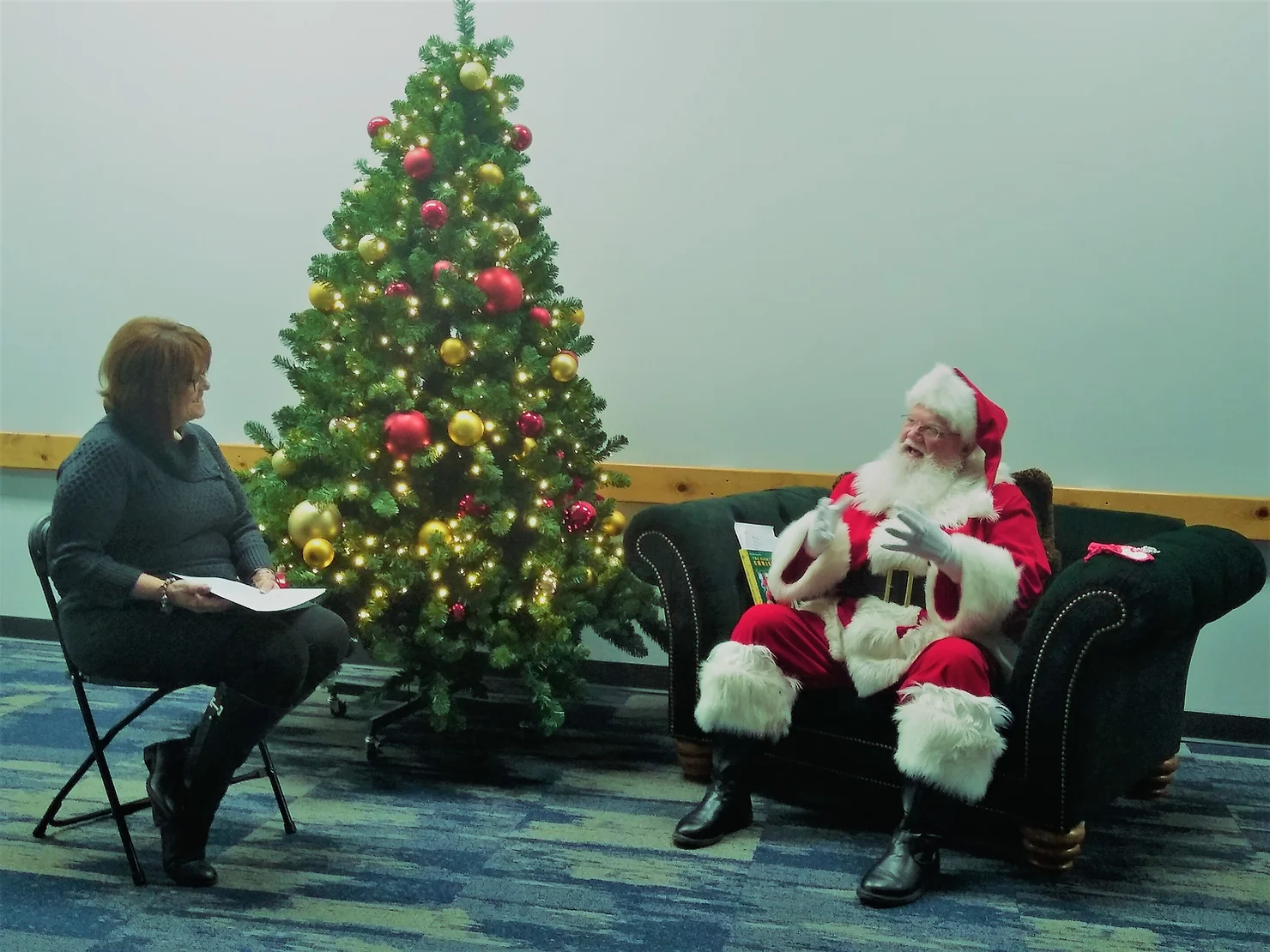 Santa being interviewed by Barbara next to a beautifully lit Christmas tree.