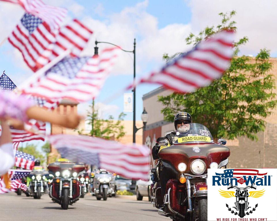 Multiple American Flags blowing in the wind during the Veterans Parade with motorcycles in the foreground.